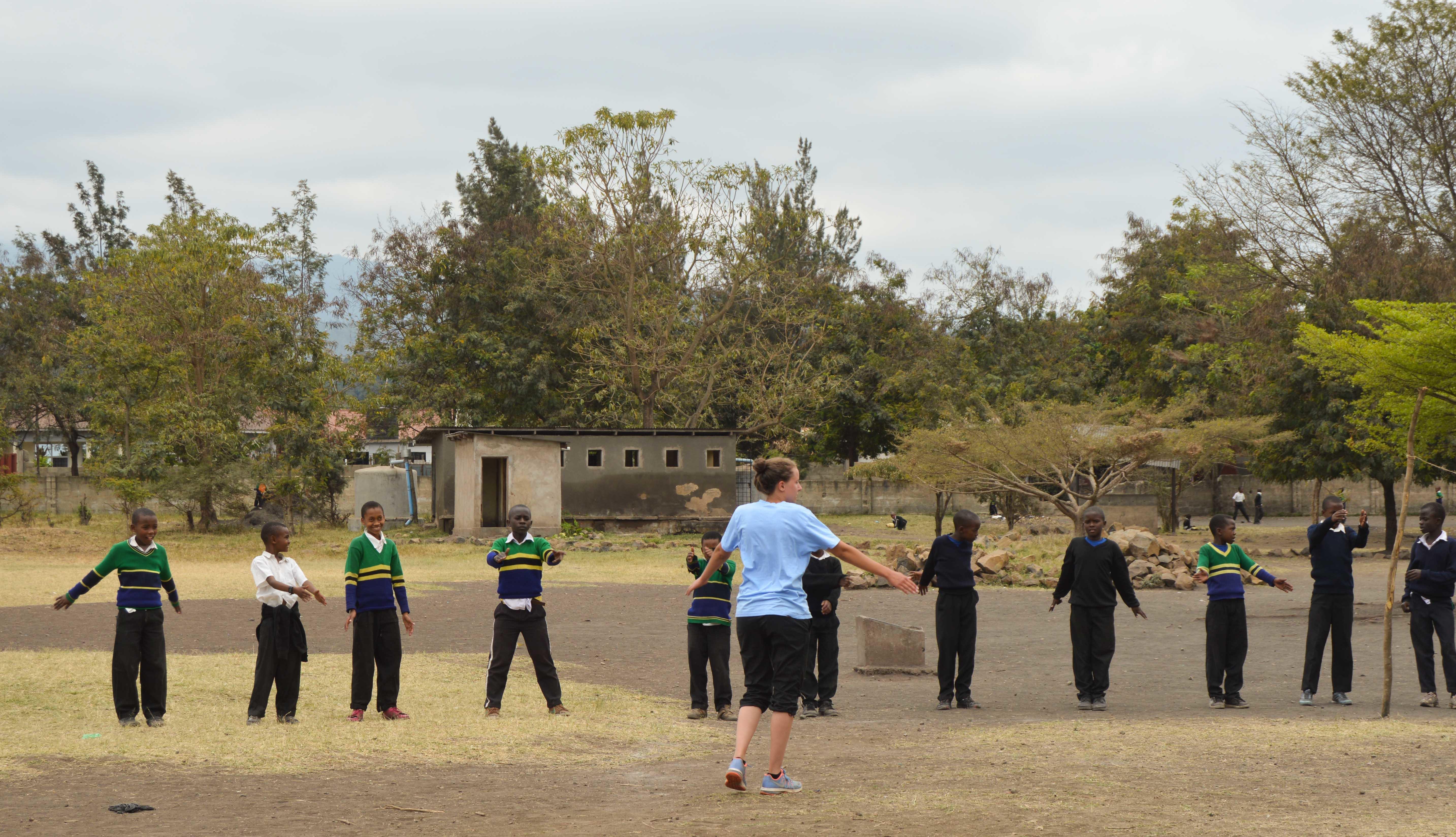 A Projects Abroad volunteer working as a sports coach in Tanzanian schools does a quick warm up before practice A sports instructor does a quick warm up with students during her volunteer sports coaching in schools in Tanzania